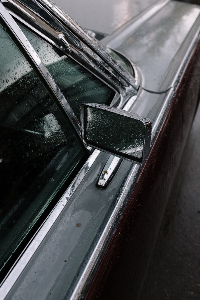 Close-up of a vintage car with raindrops on the side mirror and window, showcasing classic elegance.